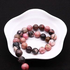 Perles rondes en rhodonite naturelle rose et noire sur une coupelle décorative blanche