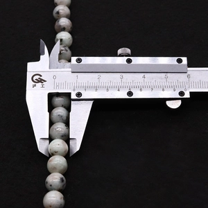 Gros plan de perles en pierre naturelle de 8 mm avec points noirs mesurées par un étrier