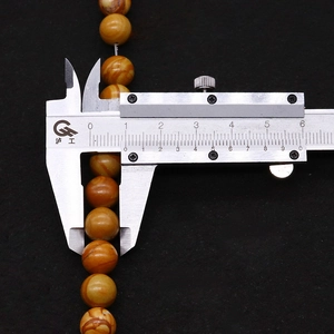 Macro view of 8mm natural wood grain stone beads being measured with a silver caliper