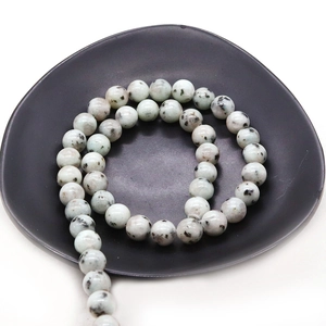 Perles rondes en pierre de kiwi naturelle avec taches noires disposées en spirale sur plateau