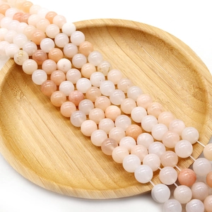 Polished natural light pink stone beads for DIY jewelry making on a wooden tray