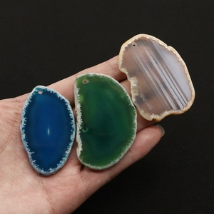 Mano che tiene tre ciondoli a fetta di agata naturale lucidata in blu verde e grigio