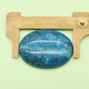 Measuring 40mm oval blue stone with brass calipers on green background