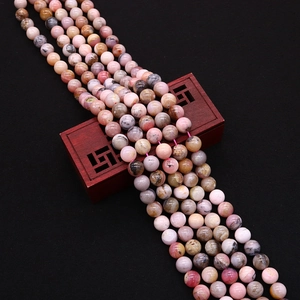 Detail of round natural pink stone beads with black textures on a wooden display