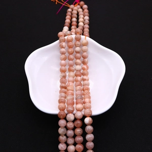 Close-up of polished natural orange sunstone round beads on white ceramic plate