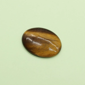 Pietra occhio di tigre cabochon ovale con lucentezza dorata su sfondo verde chiaro