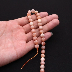 Detailed view of translucent orange sunstone round beads held in hand for jewelry DIY
