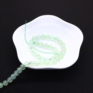 Dettaglio di perle rotonde in prehnite verde chiaro traslucido in una ciotola bianca