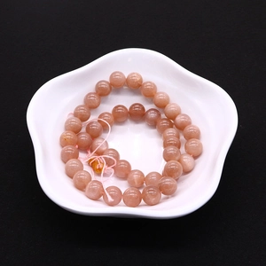 Macro shot of natural pink sunstone round beads in a white ceramic dish over black background