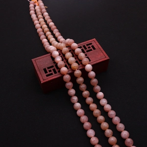 Close-up of pink natural sunstone round beads draped over a vintage red wooden box