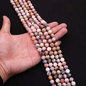 Multiple strands of natural pink opal round beads for jewelry making held in hand
