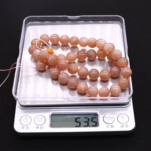 Macro shot of natural orange sunstone round beads on scale weighing 53.5 grams