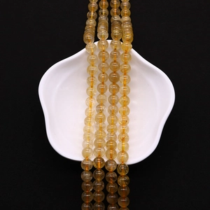 Detailed view of four golden rutilated quartz bead strands on a white porcelain dish