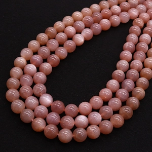 Polished peach pink sunstone beads in U-shaped arrangement on black texture background