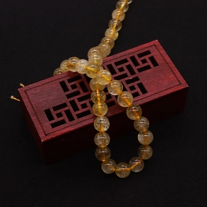 Macro shot of gold rutilated quartz beads with visible natural needle inclusions on a dark stand