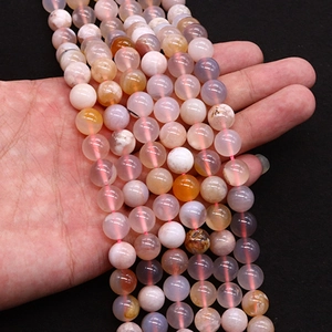 Hand holding natural cherry blossom agate beads in mixed colors of pink and purple