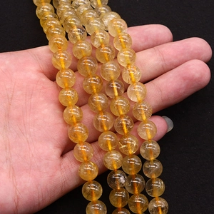 Hand holding polished yellow citrine beads with rutilated quartz needles for jewelry DIY