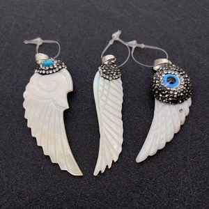 Macro detail of hand-carved shell wing pendants with evil eye and rhinestone inlay