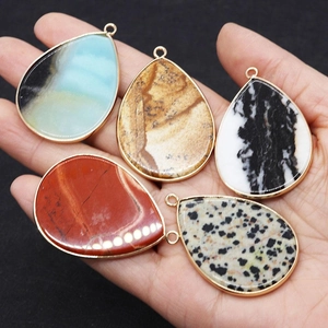Set of five teardrop natural stone pendants with gold metal edges held in hand