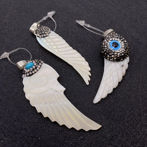 Macro shot of natural shell wing pendants with carved feathers and sparkly crystals