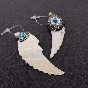 Detail of wing-shaped shell earrings with blue eye beads and crystal embellishments