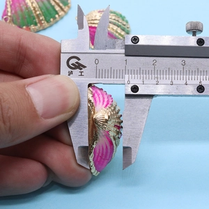 Vue macro d'un pendentif coquillage rose au bord doré mesuré par un pied à coulisse