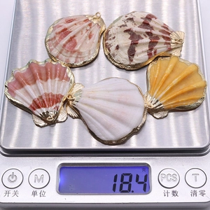 Vue détaillée de cinq pendentifs en coquillage pesés sur une balance numérique de bijoux