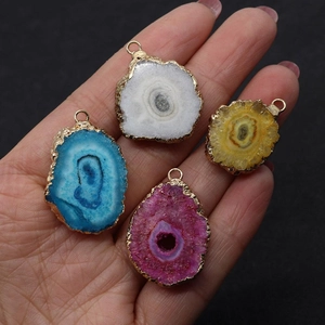 Detail of colorful irregular agate druzy pendants with gold plated edges on hand