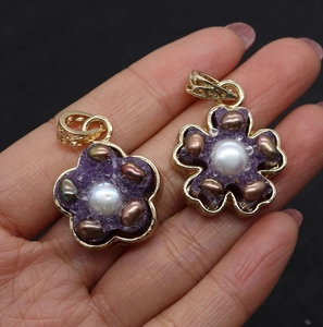 Handheld photo of golden flower charms with purple resin and natural freshwater pearl centers