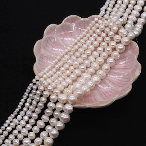 Detail of natural white freshwater pearls in various sizes displayed on a pink shell plate