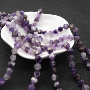 Macro detail of faceted purple amethyst beads draped over a white ceramic leaf dish