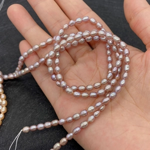 Detail of lavender rice-shaped freshwater pearls on a string held in hand for scale