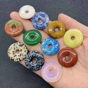 Close-up of various natural stone donut pendants held in hand showing smooth textures