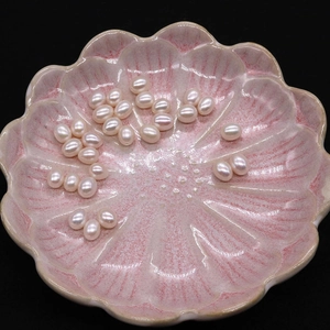 Macro detail of rice-shaped pink freshwater pearls scattered on a decorative ceramic dish