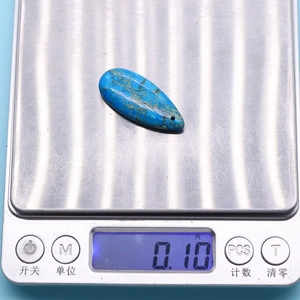 Détail d'un pendentif turquoise en forme de goutte sur une balance affichant le poids