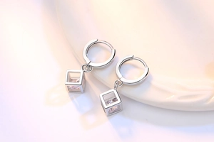 Detalle macro de pendientes de cubo plateados con circón púrpura sobre cerámica blanca