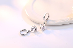 Detalle de pendientes huggie plateados con colgante de cubo geométrico y circón claro