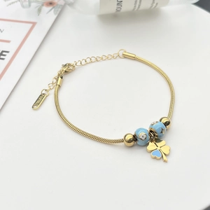 Detail von goldenem Schlangenarmband mit blauem Emaille-Kleeblatt und S.STEEL-Tag