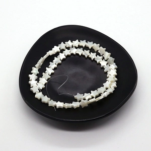 Natural white star-shaped mother of pearl shell beads arranged on a dark plate