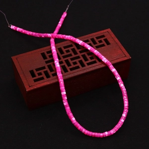 Macro shot of rose pink shell cylinder beads with iridescent luster on a dark wooden box