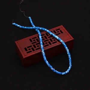 Detailed view of 2x4mm blue natural shell disk beads displayed on vintage wooden box