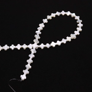Vue détaillée de perles en nacre blanche en forme de croix avec un éclat naturel sur noir