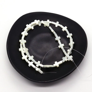 Perles en forme de croix en nacre blanche naturelle disposées en spirale sur plateau noir