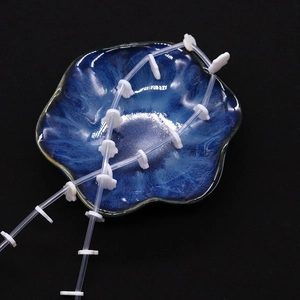Detailed view of white Hamsa hand shell beads on a blue ceramic dish with black backdrop
