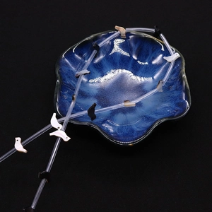 Close-up of bird shell beads and dark round beads draped over a blue ceramic bowl