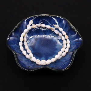 Makroaufnahme cremeweißer Muschelperlen in Reisform mit Glanz auf einer blauen Schale