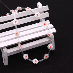 Detailed macro shot of white shell daisy beads with red centers on a white prop chair