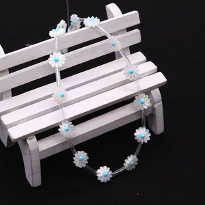Detail of daisy shell flower beads with white petals and blue centers on a white mini chair