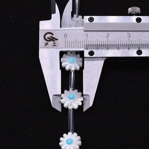 Calipers measuring a white matte daisy bead with a blue center for DIY jewelry making