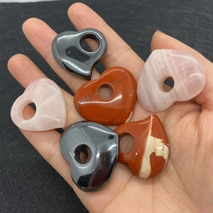 Hand met hartvormige hangers van rozenkwarts en hematiet met een centraal gat